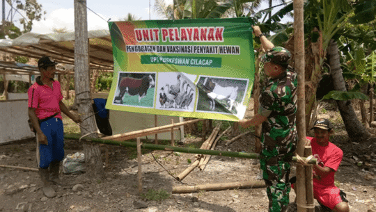 Sertu Mulyono Dan Warga Memasang Banner Untuk Posko Kesehatan Hewan