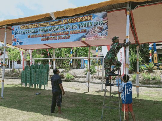 Kopda Taufik Bantu Stan Warga, Dalam Pasang Banner Pasar Murah Produk Unggulan Masyarakat Desa Cilibang