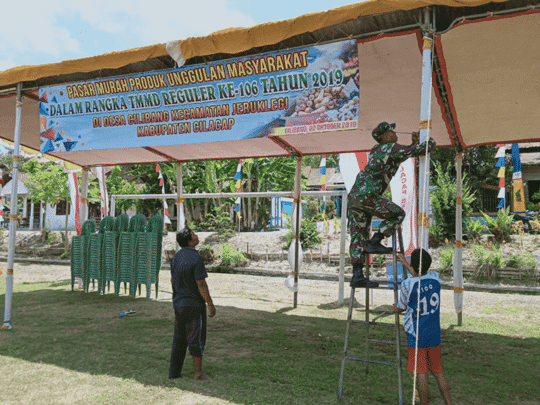 Kopda Taufik Bantu Stan Warga, Dalam Pasang Banner Pasar Murah Produk Unggulan Masyarakat Desa Cilibang