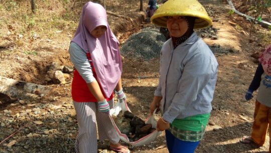 Dukung Program TMMD, Dua Orang Warga Kaligintung angkat batu krop menggunakan kandi Dan Karung